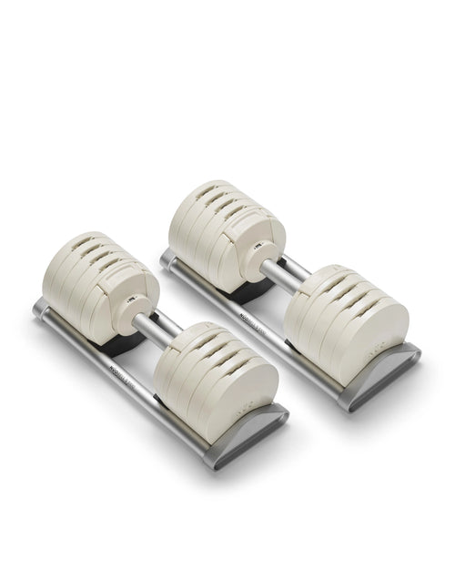 NÜOBELL S 5100 adjustable dumbbell pair in cream finish photographed at side angle on white background, displaying the individual weight plates separated along the aluminum handle to illustrate the internal stacking mechanism, stainless steel V-connectors between each disc, and the precision engineering that enables instant 5 lb adjustments from 5 to 100 lbs through the twist-handle system.