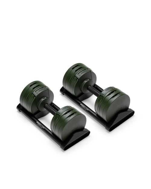 NÜOBELL S 560 adjustable dumbbell pair in dark olive green positioned on black storage cradles at a three-quarter angle, displaying the central twist-handle weight selector mechanism with visible increment markings, the four-plate shifting system with stainless steel V-connectors, and the textured 32mm aluminum handle designed for controlled grip during progressive strength training.