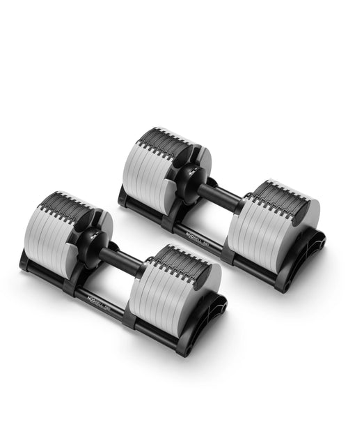NÜOBELL 580 dumbbells in black and silver finish photographed as two units positioned diagonally against a white background, showing the stacked weight plate configuration with individual selector discs visible on each cylindrical head, the central twist-handle adjustment mechanism with NÜOBELL 580 branding on the handle shaft, and the cradle base design that enables stable storage between training sets.